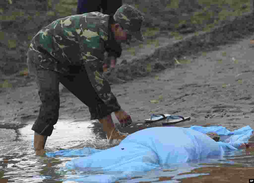 A Laotian soldier covers the body of a plane crash victim with a sheet on the bank of the Mekong River in Pakse, Laos, Oct. 18, 2013.