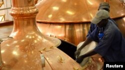 FILE - Workers pour brewing ingredients in a copper kettle at the Nile Brewery Company, east of Uganda's capital Kampala. In the slums of Kampala, friends gather to drink their cheap home made brew 'malwa'.