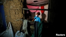 Mable Selina Etambo looks at her phone as seen through the window of her mud-walled house, as authorities around the world impose various guidelines on lockdowns and social distancing to curb the spread of COVID-19 in Kibera, Kenya May 25, 2020. (REUTERS/Thomas Mukoya)