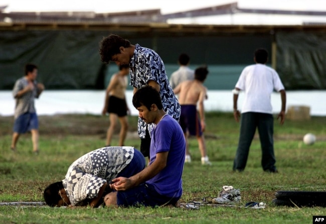 FILE - A small group of Muslim refugees pray at sunset while others play soccer at an Australian-run camp for asylum seekers on the small Pacfic island of Nauru, Sept. 20, 2001. Australia run similar camps on Manus Island in Papua New Guinea.