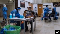 Israelis are tested for the coronavirus by health care workers at a COVID-19 testing site in Ramat Gan, Israel, Jan. 2, 2022. 