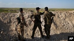 FILE - Fighters from the U.S-backed Syrian Manbij Military Council stand behind a sand barrier as they look toward a Turkish-backed fighters' position at the front line of Halawanji village, north of Manbij town, Syria, March 29, 2018. 