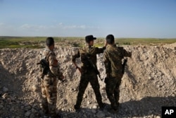 FILE - Fighters from the U.S-backed Syrian Manbij Military Council stand behind a sand barrier as they look toward a Turkey-backed fighters' position at the frontline of Halawanji village, north of Manbij, Syria, March 29, 2018.