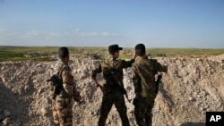 FILE -Fighters from the U.S-backed Syrian Manbij Military Council stand behind a sand barrier as they look toward a Turkish-backed fighters' position at the front line of Halawanji village, north of Manbij town, Syria, March 29, 2018. 