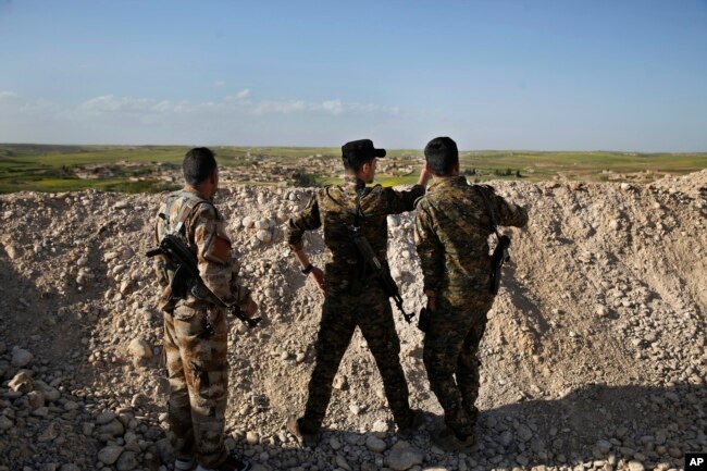 FILE - Fighters from the U.S-backed Syrian Manbij Military Council stand behind a sand barrier as they look toward a Turkey-backed fighters' position at the frontline of Halawanji village, north of Manbij, Syria, March 29, 2018.