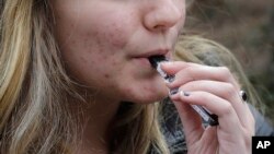 FILE - An unidentified 15-year-old high school student uses a vaping device near the school's campus in Cambridge, Massachusetts, April 11, 2018. 