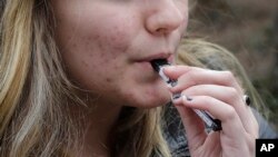 FILE - A high school student uses a vaping device near the school's campus in Cambridge, Mass., April 11, 2018. 