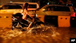 A Cambodian motorist rides a scooter through a street flooded by heavy rain fall in Phnom Penh, Cambodia, Friday, July 31, 2015. (AP Photo/Heng Sinith)