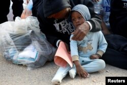 FILE - A migrant sits with her child as they wait before their voluntary return to their country, at a detention center in Tripoli, Libya, Nov. 28, 2017.