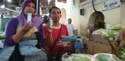 Pedagang sayur dan buah, Yatmi, dan rekannya menunjukkan hand sanitizer yang diberikan secara gratis untuk komunitas pasar tradisional di Solo, 21 Maret 2020. (Foto: VOA/Yudha Satriawan)