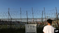 Seorang pria berjalan melewati pagar kawat berbendera nasional di dekat tanda informasi yang menunjukkan jarak ke kota Kaesong Korea Utara dan ibukota Korea Selatan, Seoul, di Paviliun Imjingak, Paju, Korea Selatan, 15 September 2017. (Foto: dok).