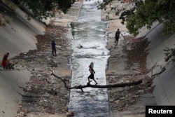 A local carries a water container as he crosses a river in Caracas, Venezuela, March 12, 2019.