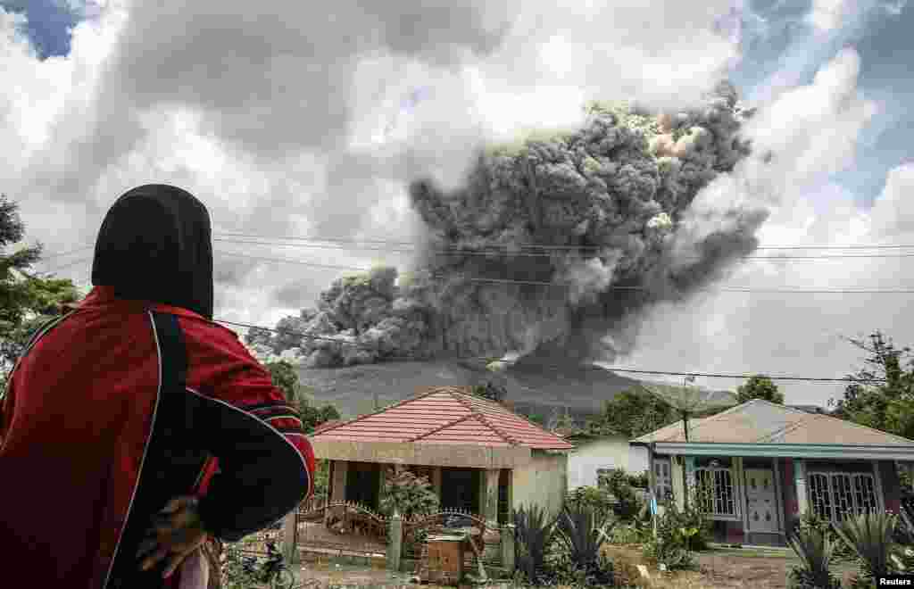 Seorang perempuan di Kabupaten Karo, Sumatera Utara mengamati letusan gunung Sinabung. 