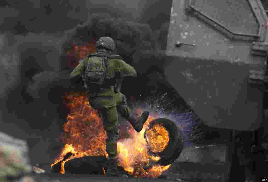 An Israeli soldier removes burning tires from the road during clashes with Palestinian protesters following a demonstration against the expropriation of Palestinian land by Israel in the village of Kfar Qaddum, near Nablus in the occupied West Bank.