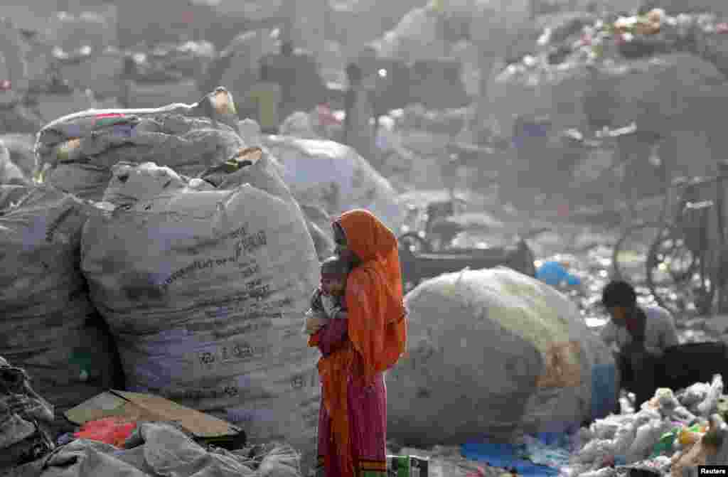 Hindistan&#39;da bir çöp yığınının yanında bir kadının, kucağındaki bebeği ile fotoğrafı çekilmiş.
