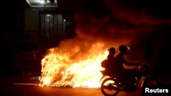 Pengendara sepeda motor melewati kobaran api di jalan ketika terjadi unjuk rasa menuntut kenaikan ongkos transportasi umum di Brazil. 
