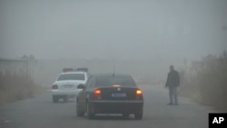 A passerby watches as a vehicle, escorted by a police car, leaves the Beijing No. 1 Detention Center on the outskirts of Beijing, China, Dec. 22, 2015.