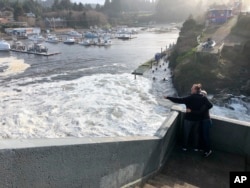 In this Jan. 11, 2020 photo residents watch as an extreme high tide rolls in and floods parts of the harbor in Depoe Bay, Oregon, USA. (AP Photo/Gillian Flaccus)