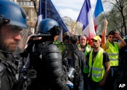 Riot police stand by as French "yellow vest" protesters rally, March 30, 2019, in Paris. The demonstrators are undeterred by protest bans or repeated injuries in 20 weeks of demonstrations.