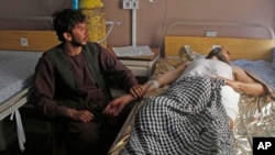 An Afghan wounded man, right, lies on the bed in a hospital as his relative sits on a chair beside him in the city of Kandahar, south of Kabul, Afghanistan, July 9, 2014. 