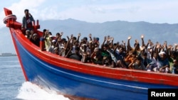 FILE - Ethnic Rohingya refugees from Burma wave as they are transported by a wooden boat to a temporary shelter in Krueng Raya in Aceh Besar.