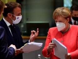 German Chancellor Angela Merkel looks into a document as France's President Emmanuel Macron gestures during the first face-to-face EU summit since the coronavirus disease (COVID-19) outbreak, in Brussels, Belgium July 20, 2020.