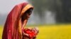FILE - Monowara holds her 22-day-old grandson Arafat, as she walks through a mustard field on the outskirts of Dhaka.