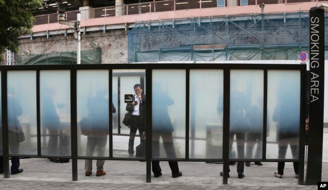 FILE - People gather at a smoking area in Tokyo, April 7, 2017.