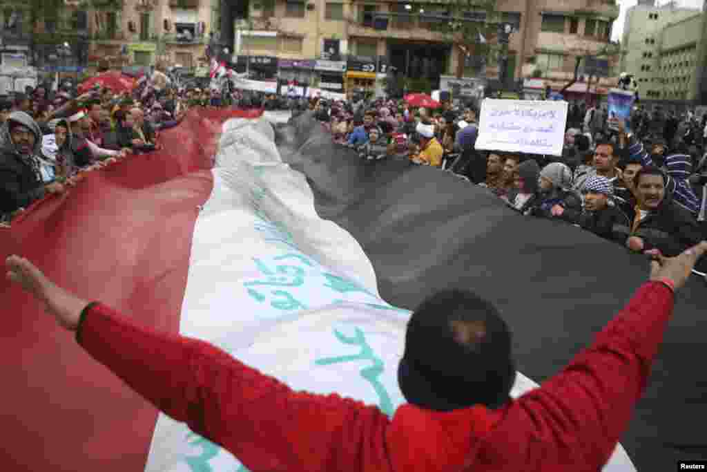 An anti-Morsi demonstrator (C) gestures to a crowd of demonstrators waving a huge Egyptian flag, after Friday prayers at Tahrir Square in Cairo, February 1, 2013.