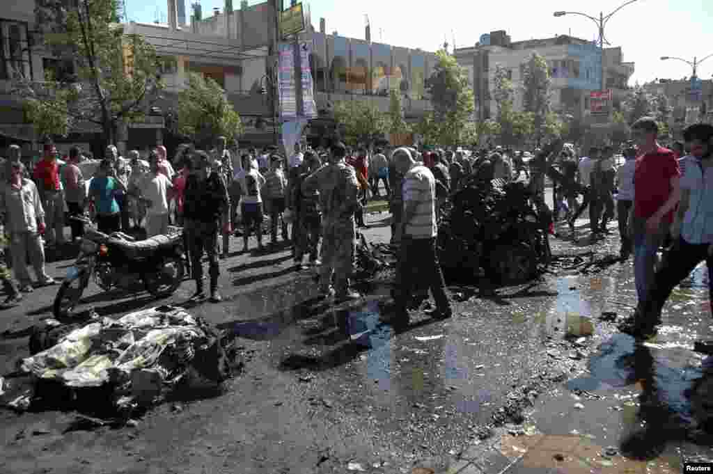 People stand at the site of an explosion in Ekrema neighborhood in Homs, Syria, July 8, 2013. (SANA)