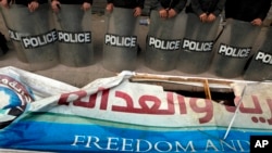 FILE - Egyptian anti-riot soldiers stand guard in front of a destroyed banner of the Muslim Brotherhood's Freedom and Justice Party, March 2013.