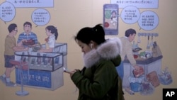 A woman browses her iPhone as she walks by a mural depicting an iPhone and Chinese people buy smartphone to communicate with family members, at a subway station in Beijing, Thursday, Jan. 3, 2019. (AP Photo/Andy Wong)