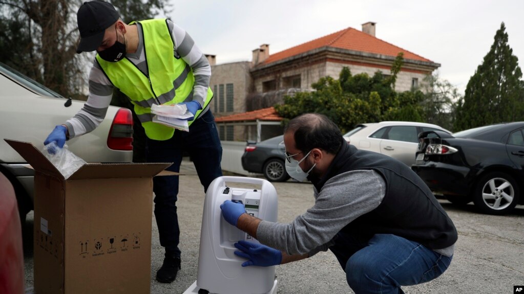 Members of Lebanese NGO Baytna Baytak Firas Minnawi, right, and Mario Suleiman, left, unpack oxygen machine to be donated to an elderly COVID-19 patient in Beit Shebab, a mountain village 15 mile (24 km) north of Beirut, Lebanon, Wednesday, Jan. 27, 2021. (AP Photo/Bilal Hussein)