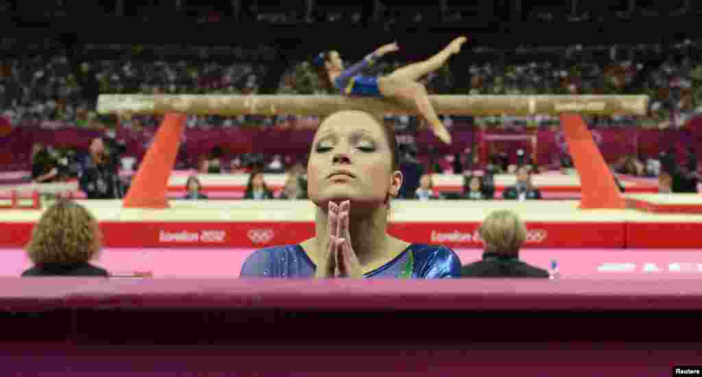 Ethiene Cristina Gonser Franco of Brazil (C) prays whilst teammate Harumy Mariko de Freitas performs on the balance beam during the women's gymnastics qualification at the North Greenwich Arena during the London 2012 Olympic Games July 29, 2012. 