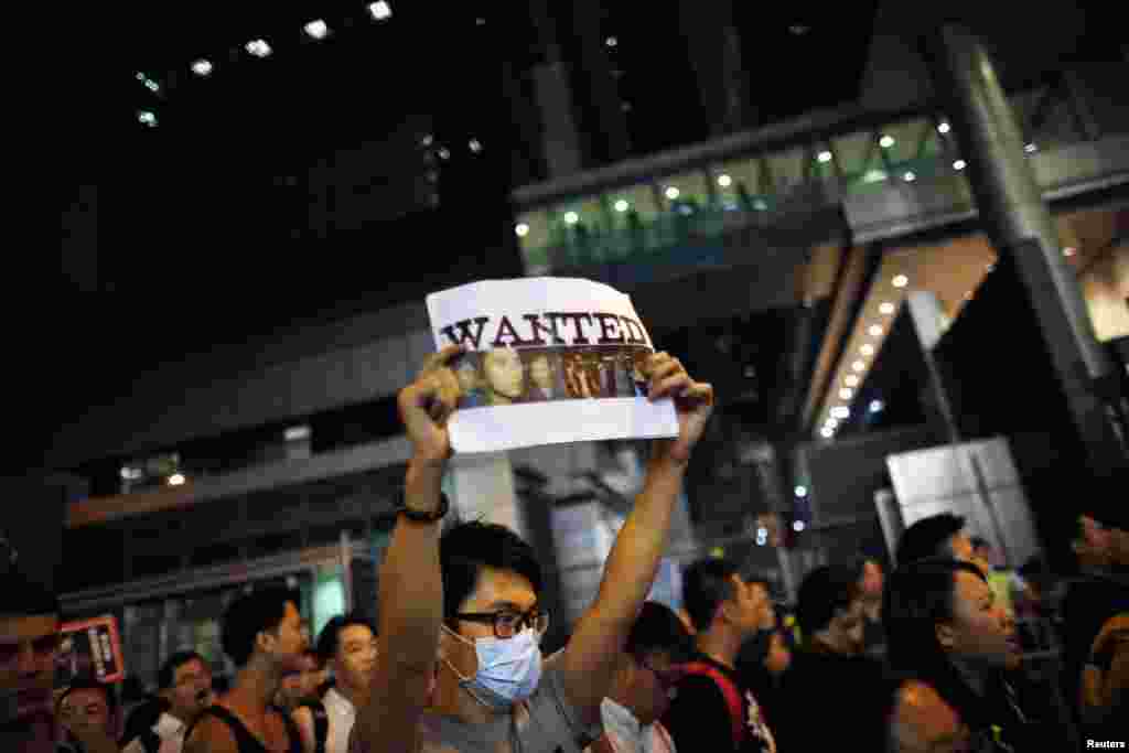 A pro-democracy protester holds a sign with pictures of police officers suspected of beating a protester at a rally last night, as he blocks the entrance of police headquarters at Wan Chai district in Hong Kong October 14, 2014. Hong Kong authorities said