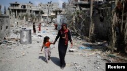 Phụ nữ Palestine dắt con đi ngang những tòa nhà bị phá hủy khi trở về thị trấn Beit Hanoun sau các vụ không kích của Israel, ngày 5/7/2014.