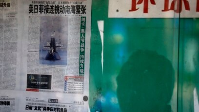 Bóng một người đàn ông Trung quốc phản ánh trên cửa kính cho thấy ông đang đọc tờ Hoàn cầu Thời báo vốn có lập trường cứng rắn và do Nhân dân Nhật báo - cơ quan ngôn luận của Đảng Cộng Sản TQ quản lý, nói về tranh chấp Biển Đông. (AP Photo/Andy Wong)