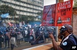 FILE - An environmental protester points his finger at the reflective window of the Ministry of Interior, as he demonstrates against recent government plans to mine coal and open a coal-fired power plant, in downtown Nairobi, Kenya, June 5, 2018.