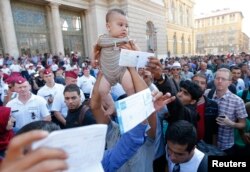 Migrants wave their train tickets and lift up children outside the main Eastern Railway station in Budapest, Hungary, Sept. 1, 2015.