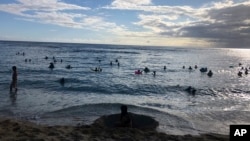 In this photo taken May 13, 2020 in Honolulu, people are in the water at a Waikiki beach. A group of people are helping track down violators of a 14-day quarantine on travelers arriving to Hawaii. (AP Photo/Jennifer Sinco Kelleher)