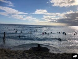 In this photo taken May 13, 2020 in Honolulu, people are in the water at a Waikiki beach. A group of people are helping track down violators of a 14-day quarantine on travelers arriving to Hawaii. (AP Photo/Jennifer Sinco Kelleher)