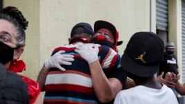 Flavio Falcone hugs a man as Andrea Macera, talks to other men as they check on people in an area known as 