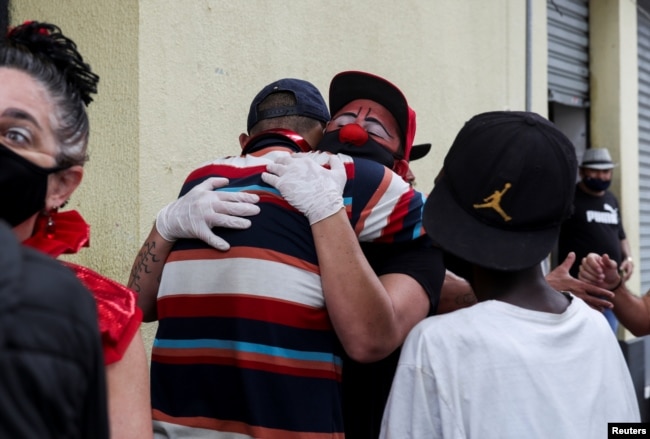 Flavio Falcone hugs a man as Andrea Macera, talks to other men as they check on people in an area known as "cracolandia" in the historic center of Sao Paulo, Brazil, February 9, 2021. REUTERS/Amanda Perobelli