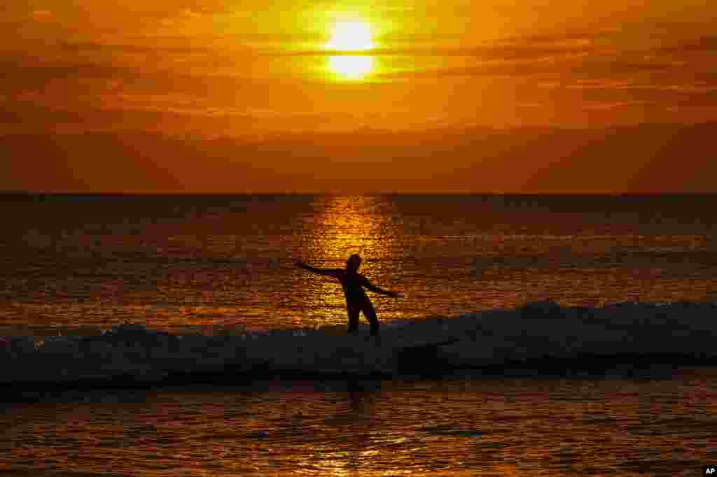 A surfer rides a waves as the sun sets in Fujisawa, Japan.