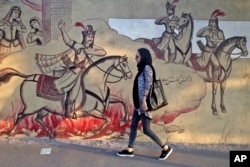 An Iranian woman walks past paintings of a Persian poetry in downtown Tehran, Iran, Monday, July 30, 2018. Iran's currency has dropped to a record low ahead of the imposition of renewed American sanctions, with many fearing prolonged economic suffering or possible civil unrest.