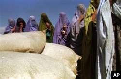 FILE - A group of women wearing burqas, most of them widows, await food aid at a distribution center run by the International Committee of the Red Cross in Kabul, Afghanistan, Oct. 13, 1996.