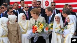 German Chancellor Angela Merkel, center, accompanied by EU Council President Donald Tusk, right, talks to young women during a visit to the Nizip refugee camp in Gaziantep province, southeastern Turkey, April 23, 2016. 