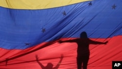 Las siluetas de manifestantes anti gubernamentales en Venezuela son vistas a través de una bandera venezolana durante una protesta en Caracas, Venezuela.