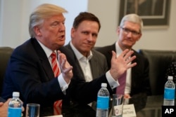 ປະທານບໍລິສນັດ Apple ທ່ານ Tim Cook, ຂວາ, ແລະເຈົ້າຂອງ ຜູ້ກໍ່ຕັ້ງບໍລິສັດ PayPal ທ່ານ Peter Thiel, ກາງ, ກຳລັງຟັງປະທານາບໍດີສະຫະລັດ ທີ່ຖືກເລືອກ ທ່ານ Donald Trump ທີ່ຖະແຫຼງໃນການພົບປະກັນທາງດ້ານເທັກໂນໂລຈີ ທີ່ຕຶກ Trump Tower ໃນນະຄອນ New York, 14 ທັນວາ, 2016.
