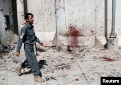 FILE - An Afghan policeman walks past a bloodstained wall after Taliban fighters stormed a government compound in Kandahar province, July 9, 2014.